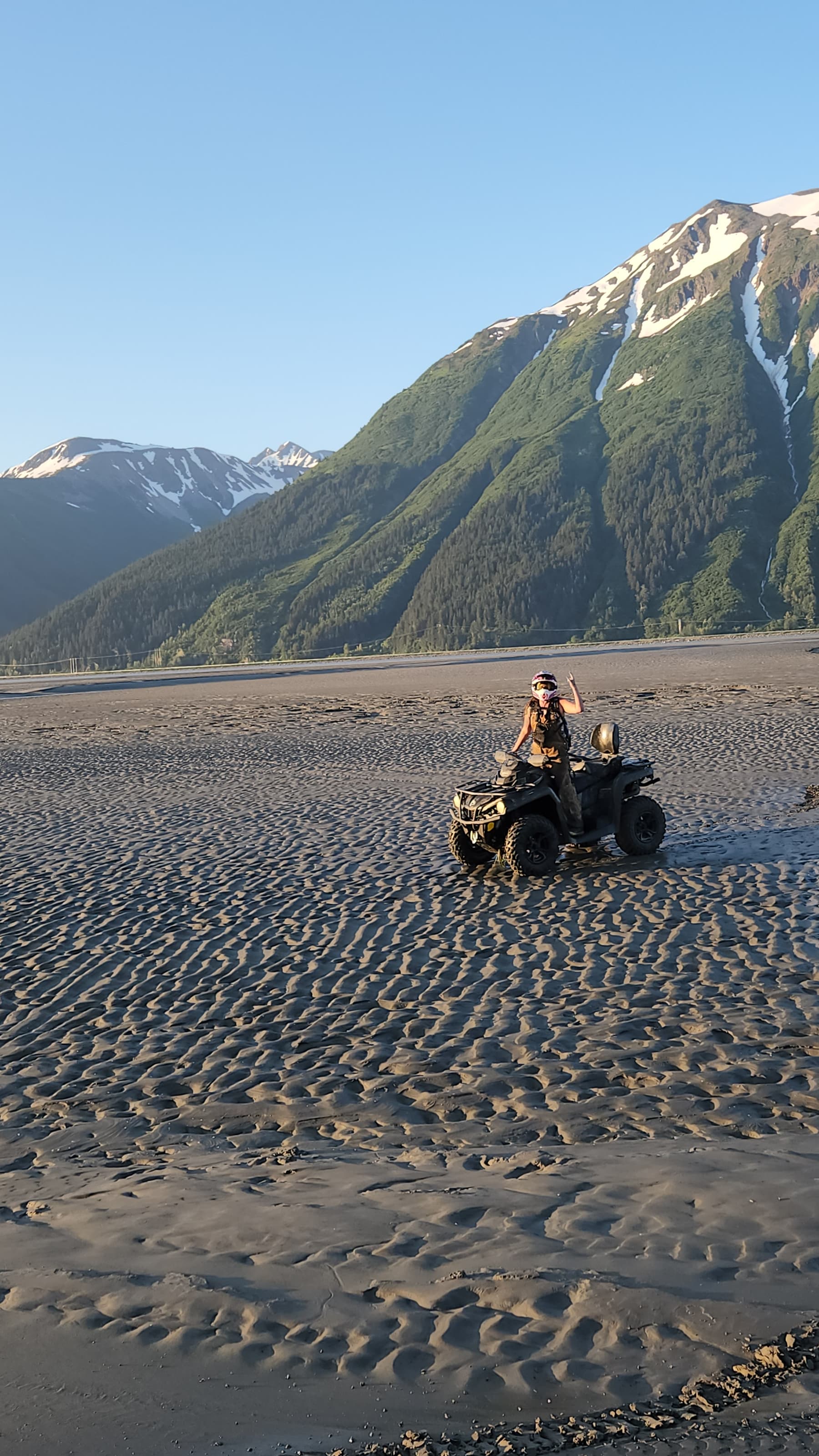 An ATV rider on golden Alaska sand flats below green mountains at sunset.